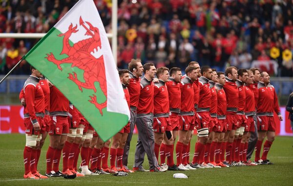 Welsh rugby team in red shirts with Welsh dragon flag on left